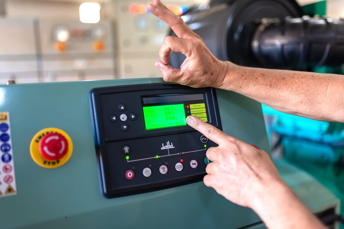 Operario manejando el panel de control de una máquina junto a la seta de emergencia