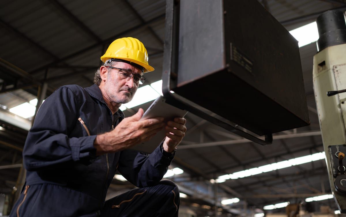 Técnico con casco y tableta revisando una máquina industrial en la nave
