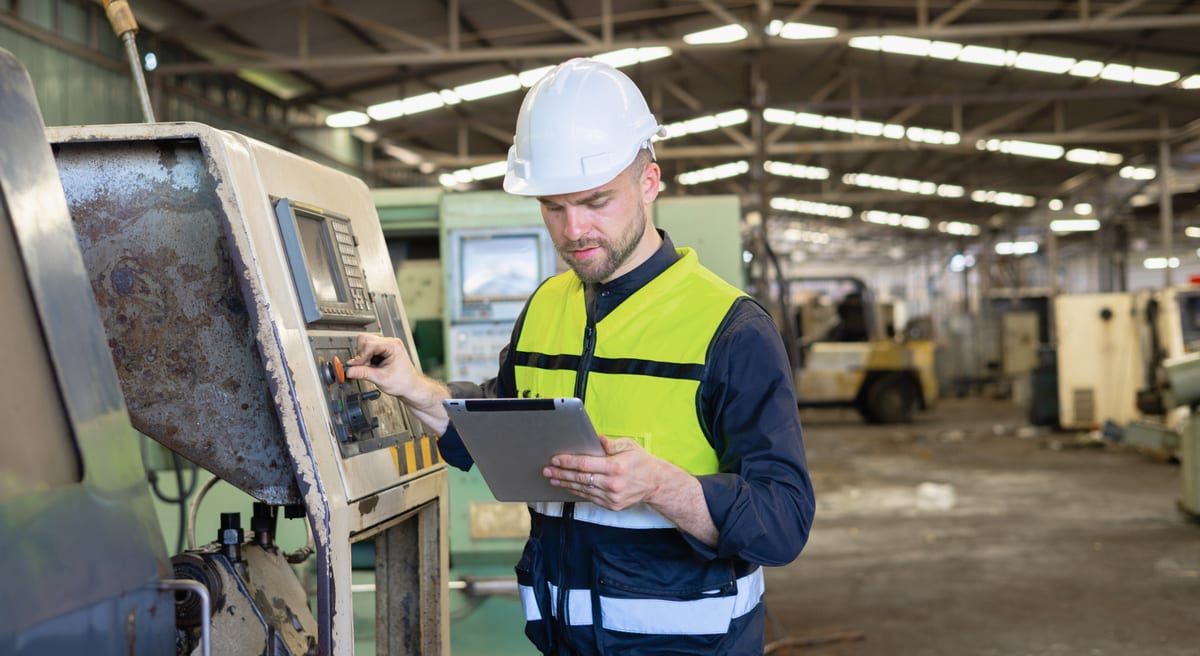 Técnico con casco revisando los mandos de una máquina con una tableta